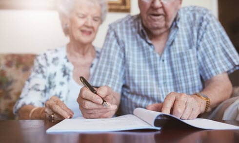 Elderly couple reviewing and signing documents at home, representing risks of financial abuse and scams targeting seniors